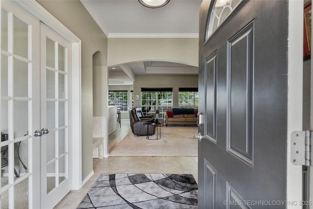 foyer with light tile patterned floors, ornamental molding, arched walkways, french doors, and light colored carpet