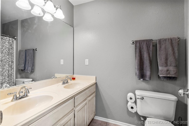 bathroom featuring toilet, double vanity, a sink, and baseboards