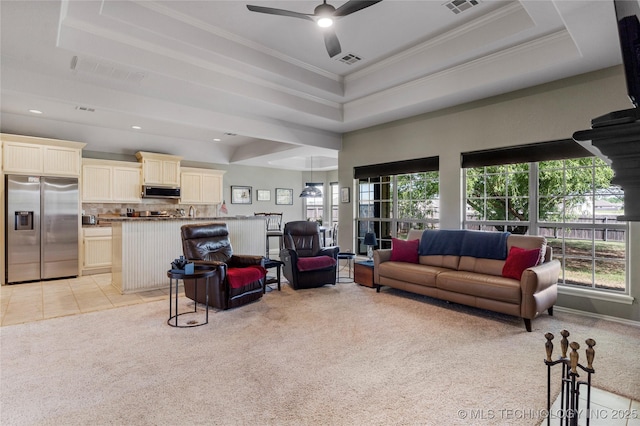 living area with visible vents, a raised ceiling, a healthy amount of sunlight, and light colored carpet