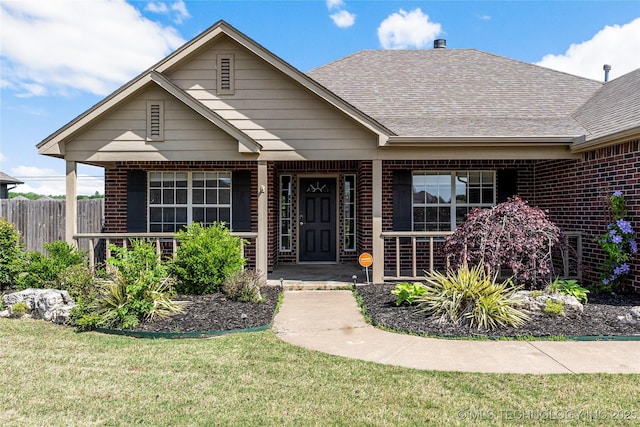 view of front of property featuring roof with shingles, a front lawn, a porch, and brick siding