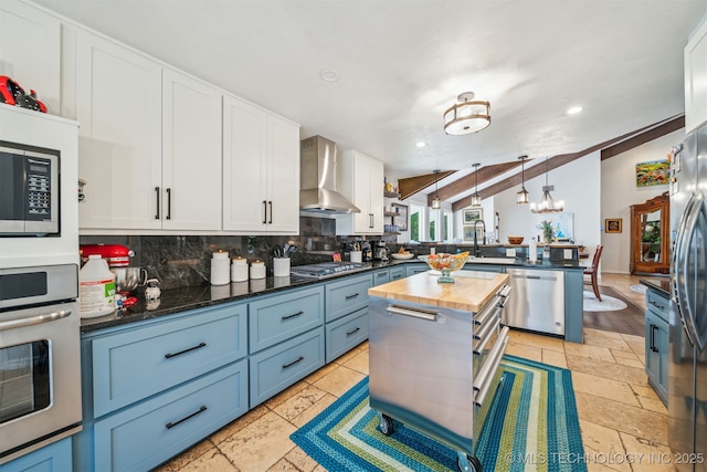 kitchen with butcher block countertops, a peninsula, stainless steel appliances, backsplash, and wall chimney exhaust hood