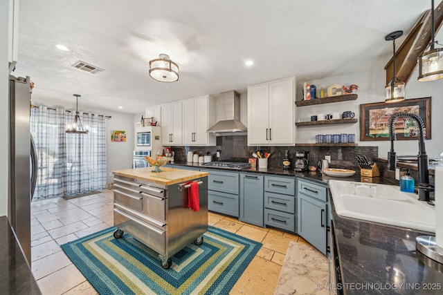 kitchen featuring wood counters, a sink, appliances with stainless steel finishes, visible vents, and wall chimney exhaust hood