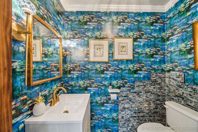 half bathroom featuring tile walls, vanity, toilet, ornamental molding, and wallpapered walls