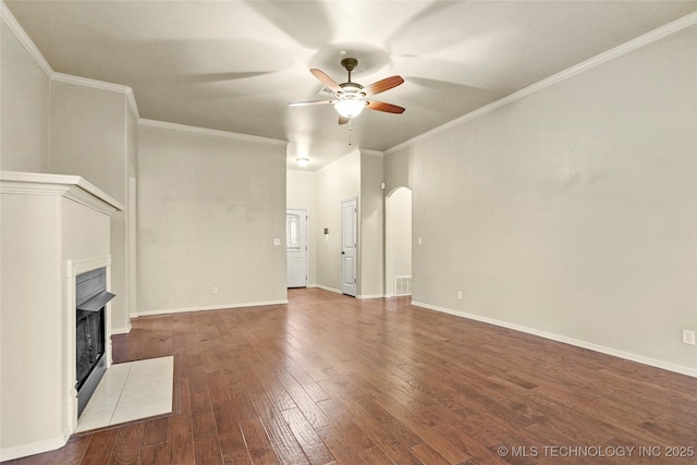 unfurnished living room featuring arched walkways, a ceiling fan, a fireplace with flush hearth, dark wood-type flooring, and ornamental molding