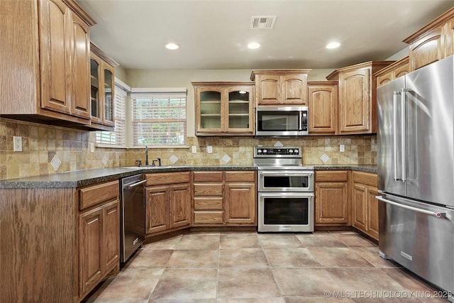 kitchen with a sink, glass insert cabinets, dark countertops, and stainless steel appliances