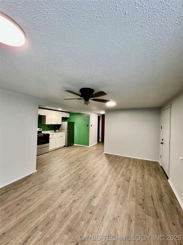unfurnished living room with a textured ceiling, light wood-type flooring, a ceiling fan, and baseboards