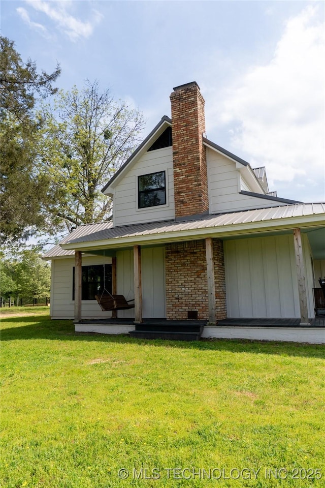 rear view of house with a chimney, board and batten siding, metal roof, and a yard