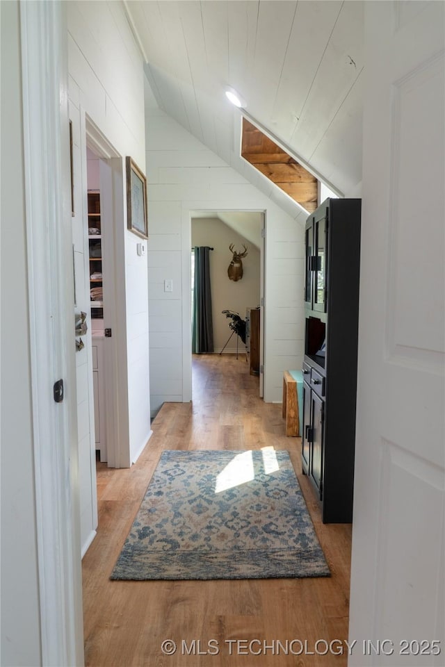 corridor with lofted ceiling, wood walls, and light wood finished floors
