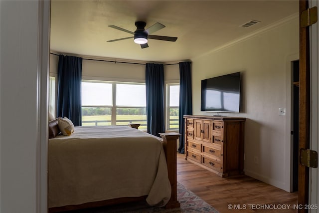 bedroom with crown molding, a ceiling fan, visible vents, baseboards, and wood finished floors