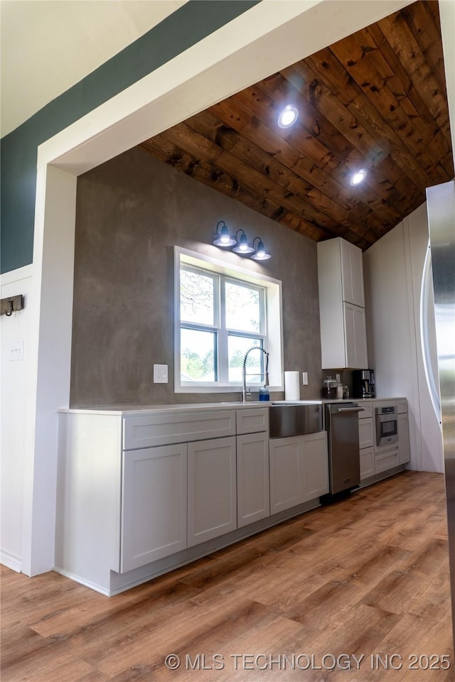 kitchen featuring a sink, light wood-type flooring, vaulted ceiling, wood ceiling, and appliances with stainless steel finishes