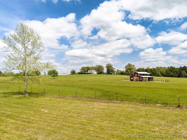 view of yard featuring fence, an outdoor structure, and a rural view