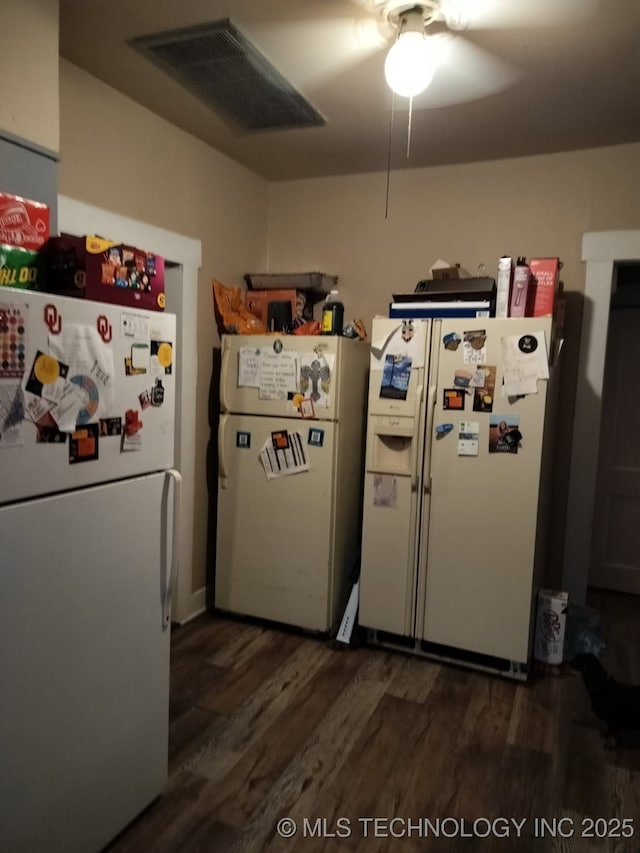 kitchen featuring dark wood-type flooring, white fridge with ice dispenser, visible vents, and freestanding refrigerator