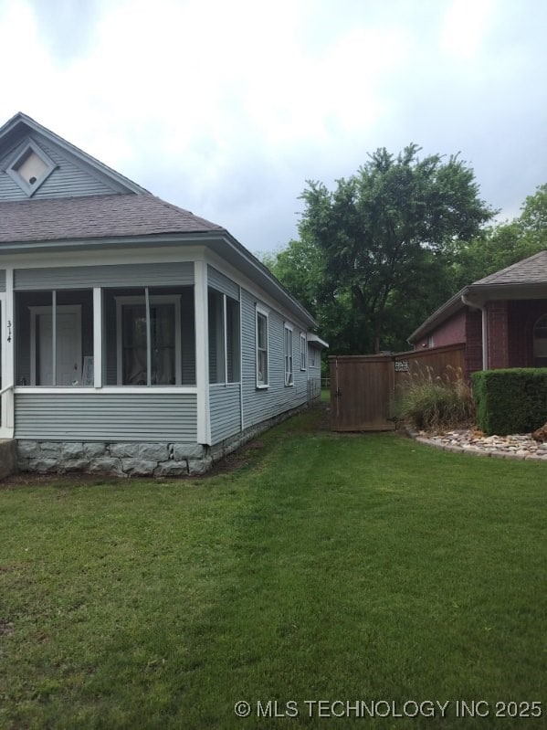 view of property exterior with a sunroom, a yard, and a shingled roof