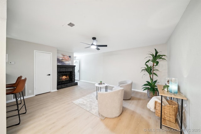 living area with baseboards, wood finished floors, a ceiling fan, and a warm lit fireplace