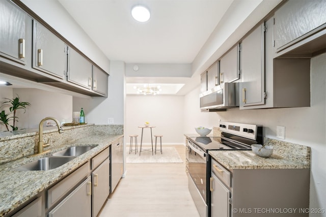 kitchen with gray cabinetry, light wood-type flooring, appliances with stainless steel finishes, and a sink