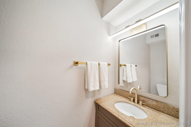 bathroom with toilet, visible vents, and vanity