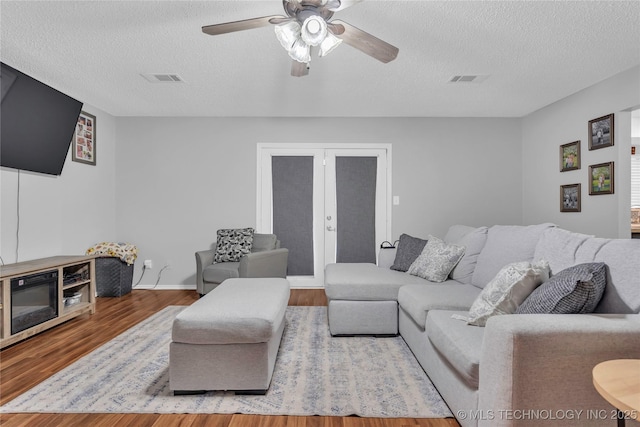 living area featuring wood finished floors, visible vents, a ceiling fan, a textured ceiling, and french doors