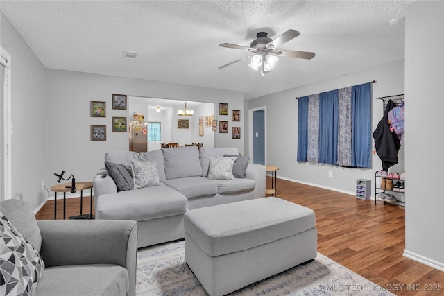 living room featuring a textured ceiling, ceiling fan, visible vents, baseboards, and wood finished floors
