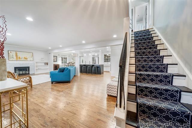 staircase with recessed lighting, a glass covered fireplace, and wood finished floors