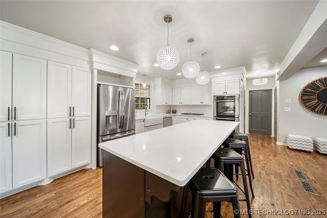 kitchen with a kitchen island, stainless steel appliances, white cabinets, and light wood-type flooring