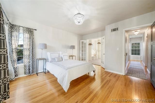 bedroom with baseboards, a notable chandelier, light wood-style flooring, and visible vents