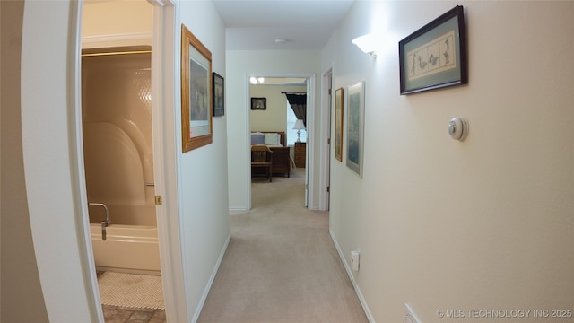 hallway featuring light colored carpet and baseboards