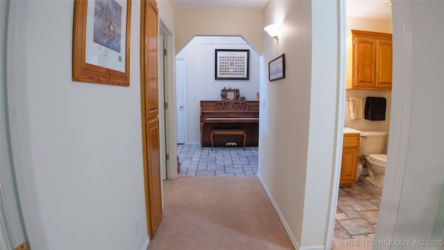 hallway featuring arched walkways, light colored carpet, and baseboards