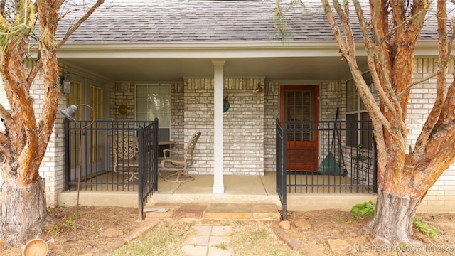 property entrance with a shingled roof, covered porch, and brick siding