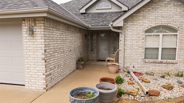 entrance to property with brick siding, a shingled roof, and a garage