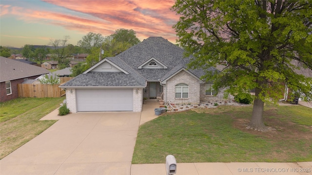 view of front of house featuring brick siding, a yard, driveway, roof with shingles, and fence