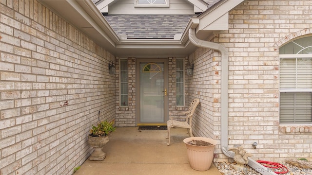 view of exterior entry with brick siding and a shingled roof