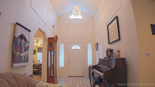 entryway with stone tile floors, high vaulted ceiling, and ceiling fan with notable chandelier