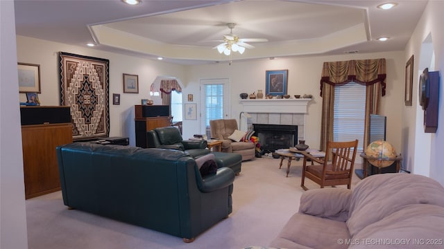 living room featuring ceiling fan, light colored carpet, a raised ceiling, and a tiled fireplace