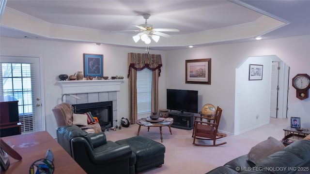 carpeted living room with ornamental molding, arched walkways, ceiling fan, and a tray ceiling