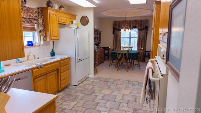 kitchen featuring a sink, stone finish floor, light countertops, stainless steel dishwasher, and freestanding refrigerator