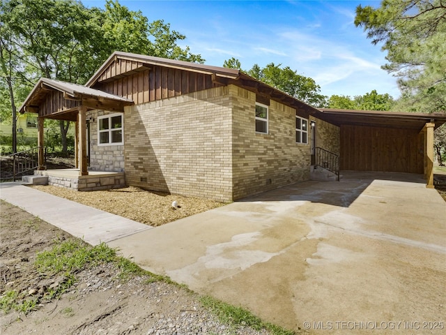 view of property exterior with brick siding, a carport, board and batten siding, and concrete driveway