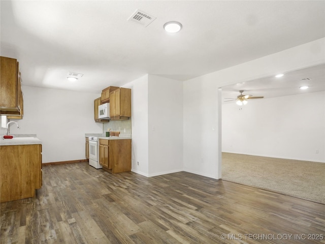 kitchen with a sink, white appliances, light countertops, brown cabinetry, and visible vents
