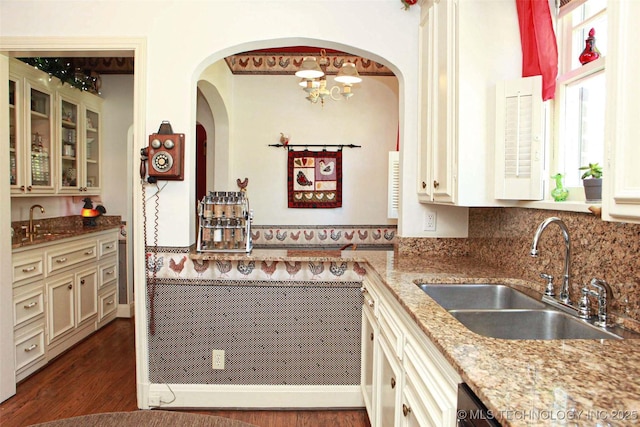 kitchen with dark wood-style floors, arched walkways, glass insert cabinets, and a sink