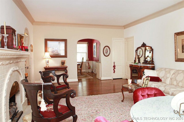 living room with a brick fireplace, arched walkways, ornamental molding, and wood finished floors