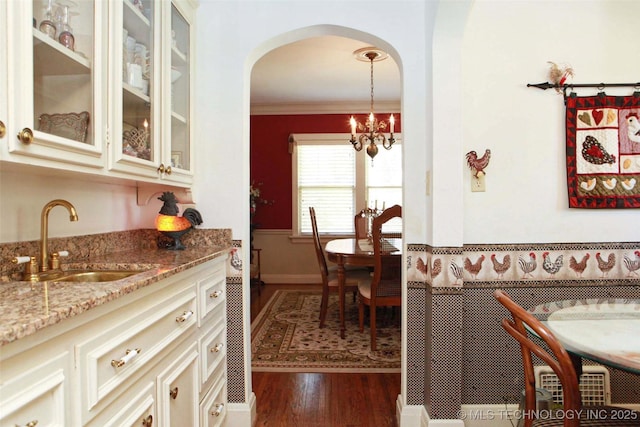 dining room with a notable chandelier, wet bar, ornamental molding, arched walkways, and wood finished floors