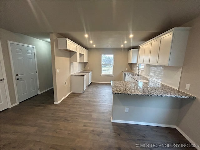 kitchen featuring stone counters, a peninsula, a sink, and baseboards