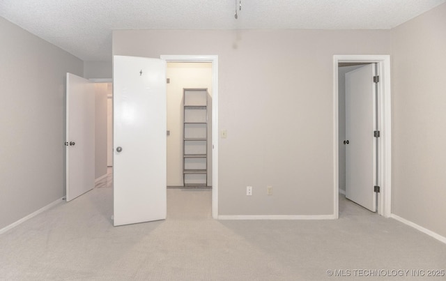 unfurnished bedroom with light colored carpet, baseboards, a textured ceiling, and a walk in closet