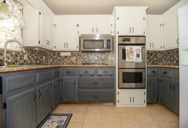 kitchen with a sink, decorative backsplash, stainless steel appliances, gray cabinets, and white cabinetry