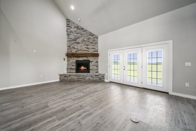 unfurnished living room featuring a stone fireplace, wood finished floors, and high vaulted ceiling