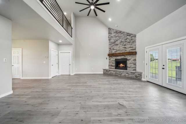 unfurnished living room featuring wood finished floors, a fireplace, high vaulted ceiling, french doors, and a ceiling fan