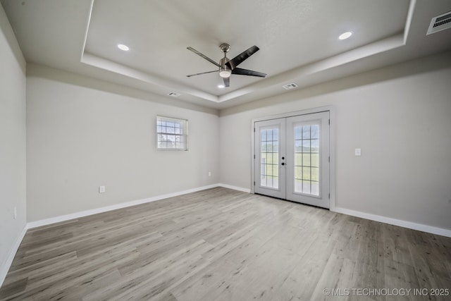 empty room with ceiling fan, french doors, visible vents, light wood-type flooring, and a tray ceiling