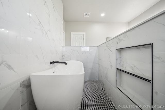 full bath featuring a freestanding bath, tile walls, and visible vents