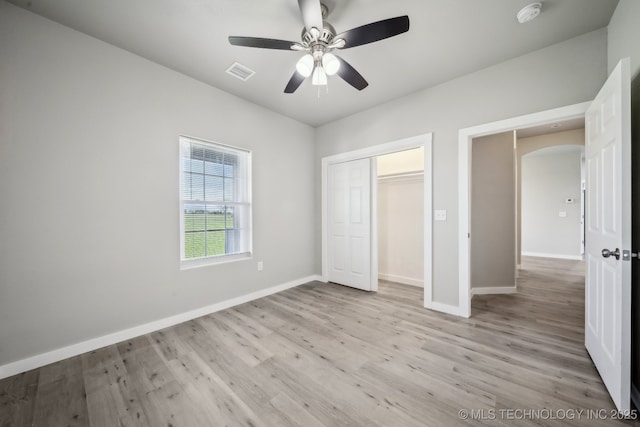 unfurnished bedroom with visible vents, a closet, light wood-style floors, baseboards, and arched walkways