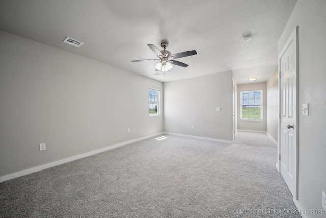 unfurnished room with visible vents, carpet, ceiling fan, and a healthy amount of sunlight