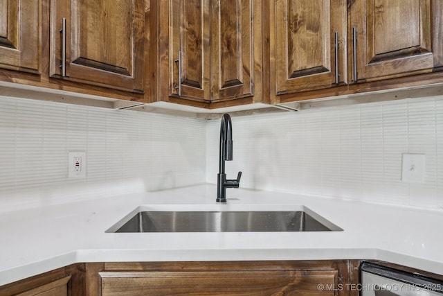 kitchen view of a sink, tasteful backsplash, light countertops, and dark brown cabinetry